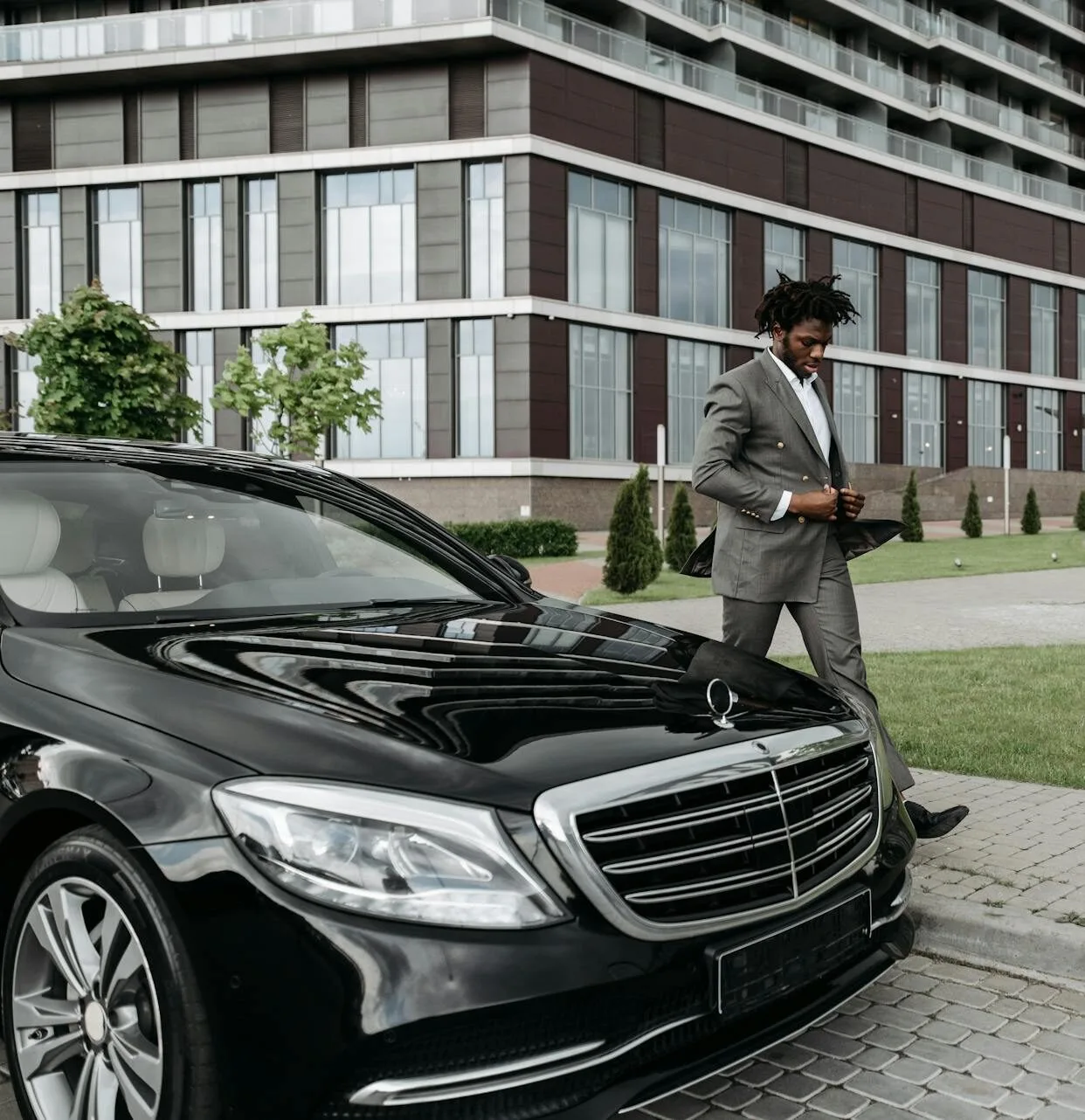 Businessman in a suit walking beside a luxury car outside a modern office