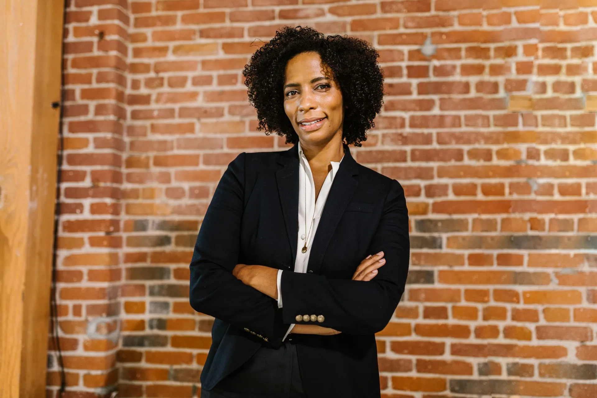 Confident female leader with arms crossed in front of a brick wall