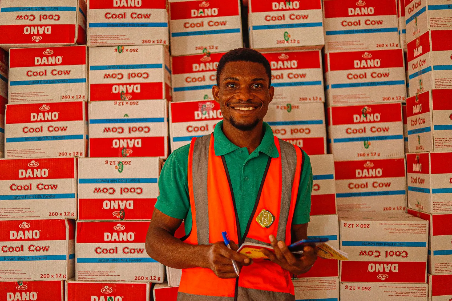 Warehouse supervisor smiling while holding a notepad in front of stacked inventory boxes